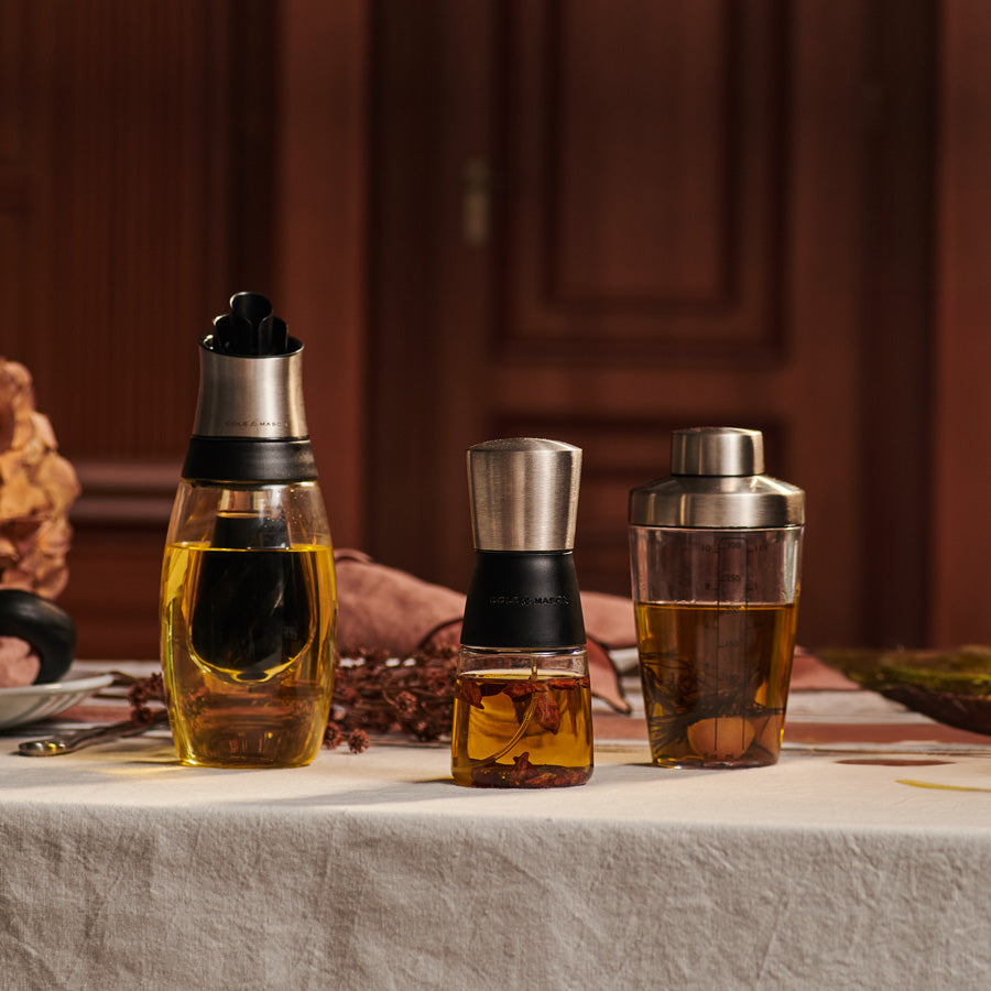 The Cole & Mason 3 Piece Oil & Vinegar Set features kitchen pourers with silver lids—one short and round, one with yellow liquid, and one marked for measurements, making it a stylish bundle of essentials.