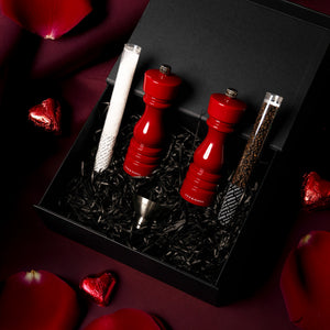 The London Red Gloss Mill Gift Hamper by Cole & Mason features a striking red gloss salt & pepper mill set, metal funnel, two seasoning tubes, rose petals, and heart-shaped chocolates—all beautifully arranged for a standout gift.